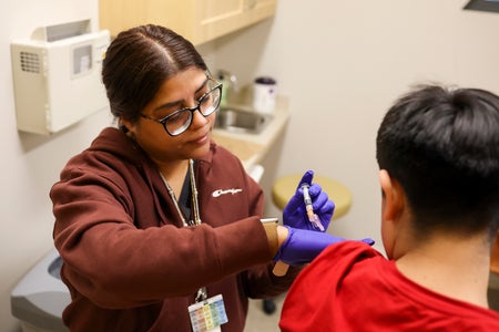 A medical assistant administers a vaccine in a patient's left arm