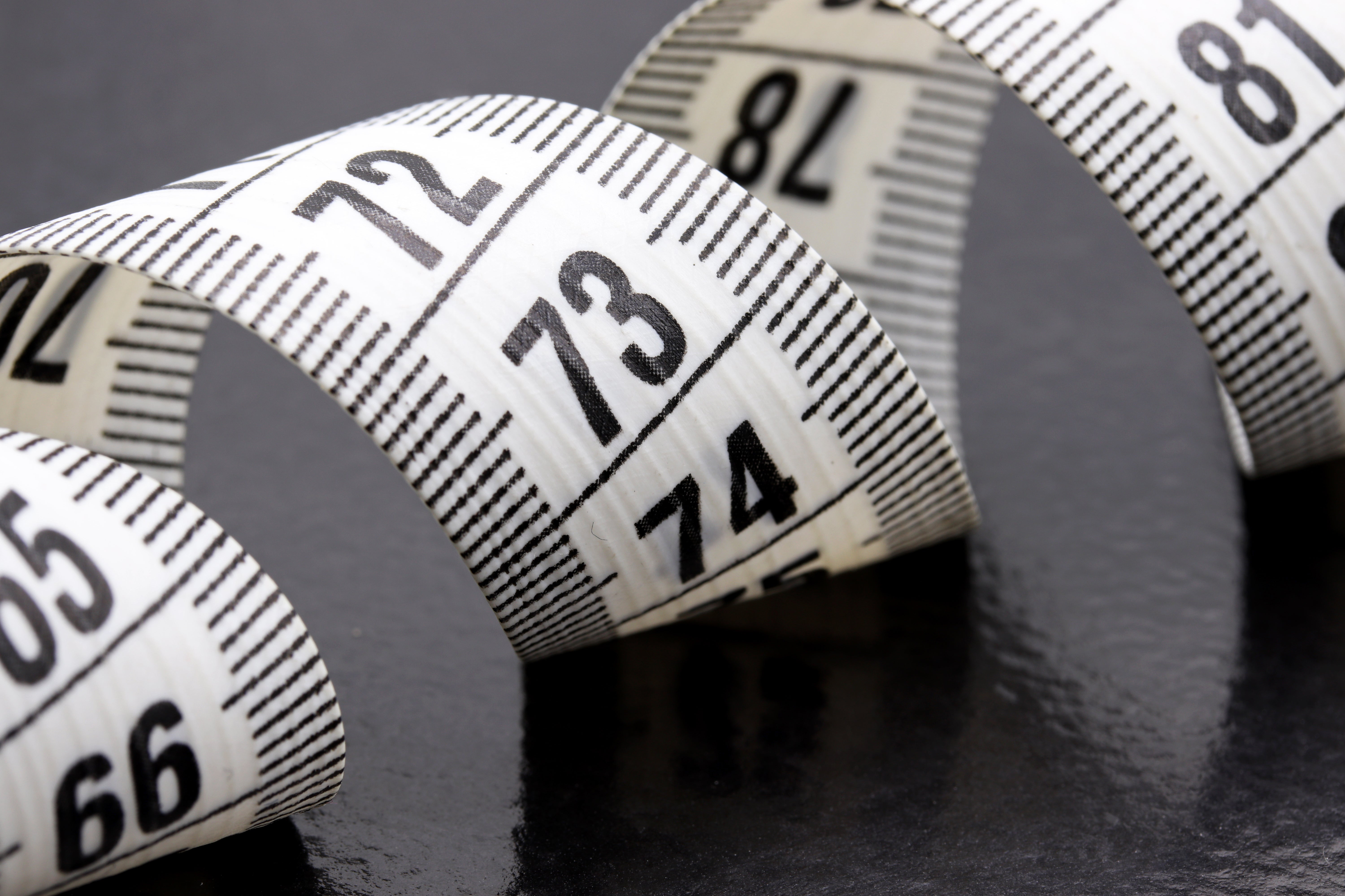Curled white tape measure on grey surface.