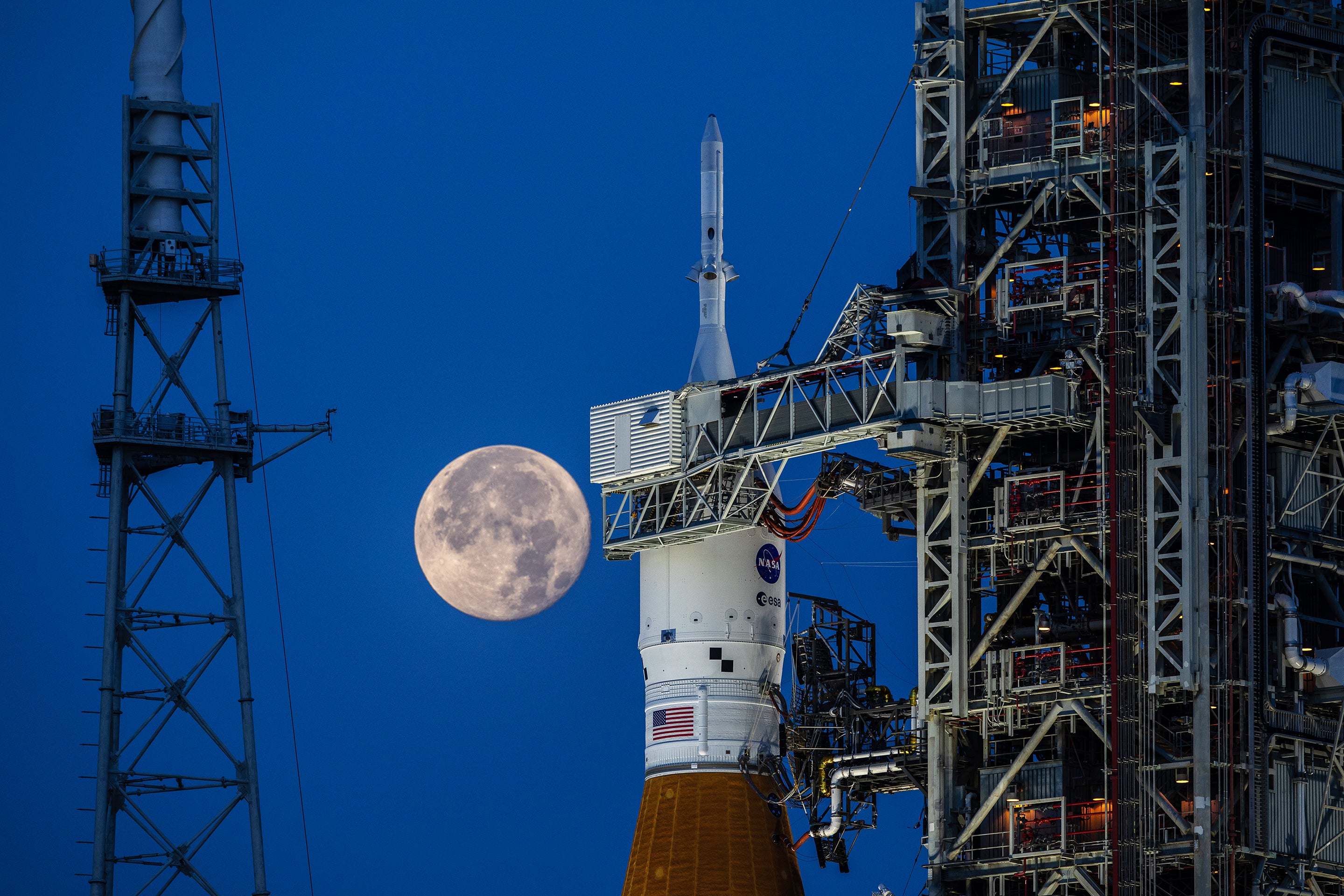 A full Moon in view behind the The Artemis I Space Launch System (SLS) and Orion spacecraft atop the mobile launcher during dress rehearsals at NASA’s Kennedy Space Center