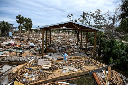 A person walking through rubble of a destroyed home.