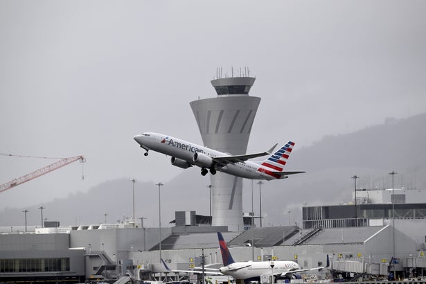 An airport scene showing a departing airplane in front of a control tower.
