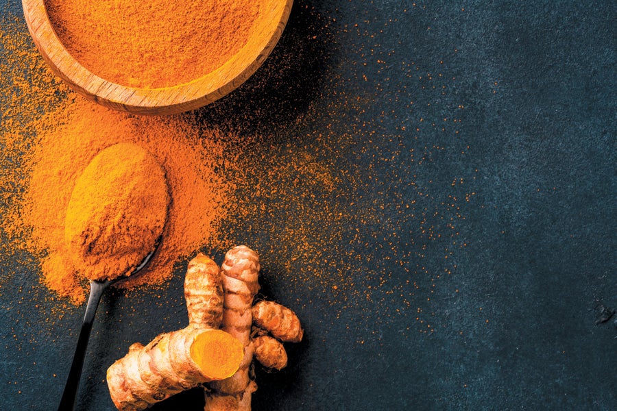 Still life of turmeric root and ground tumeric in a bowl with a spoon