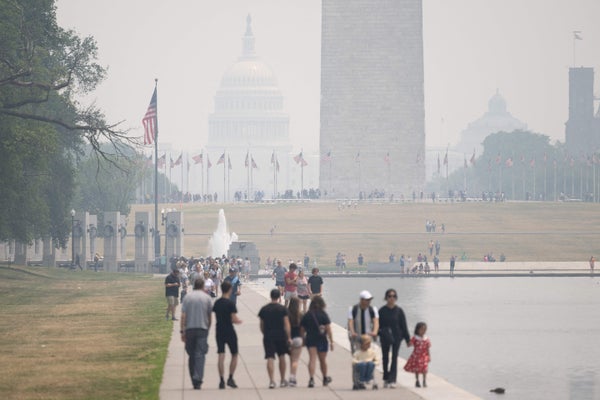 Groups of tourists walk along the reflecting pool on the National Mall near the Washington Monument amongst a thick haze of wildfire smoke. The US Capitol Building is barely visible in the distance through the smoke