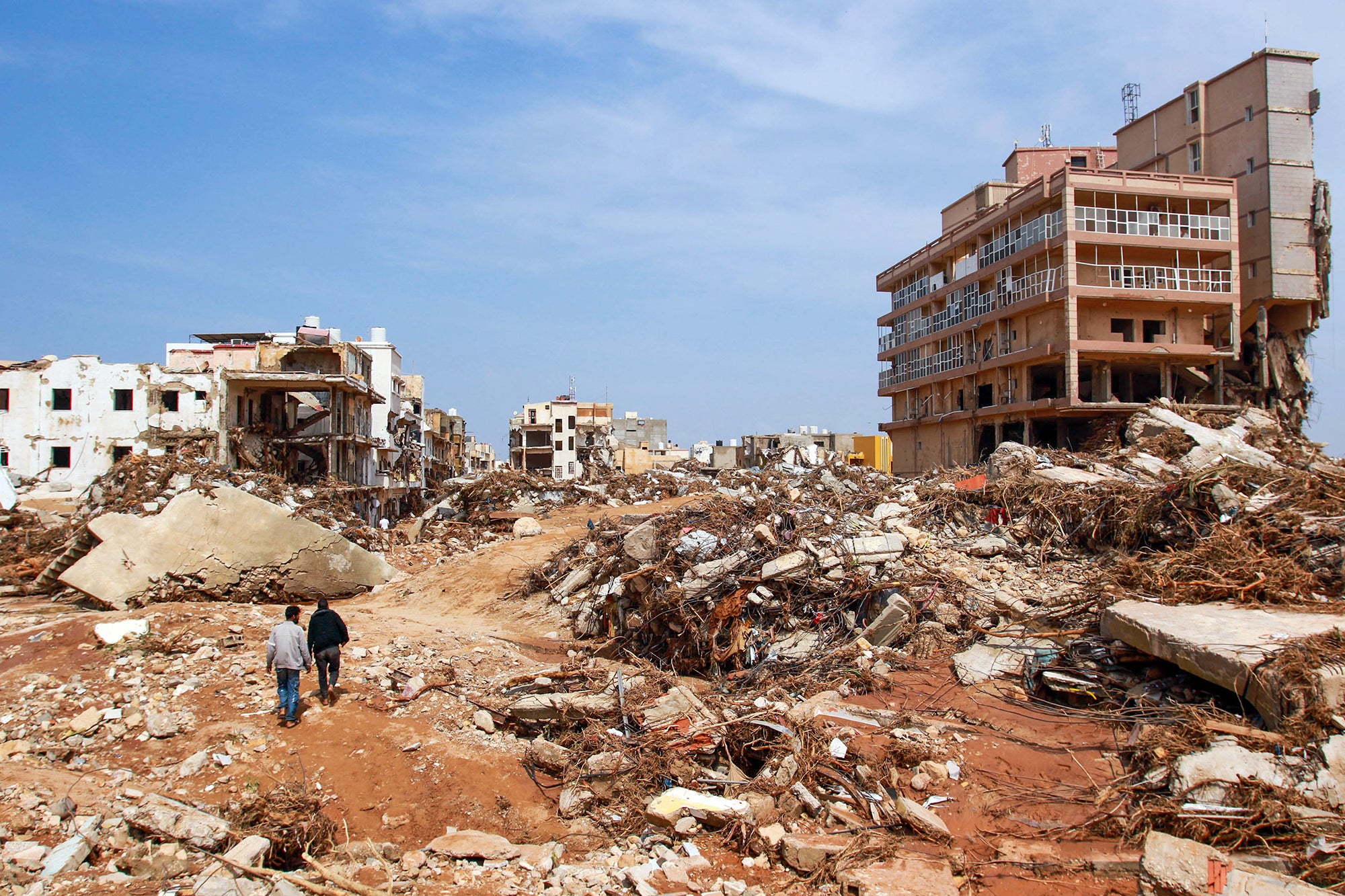Two men walk through rubble of destroyed buildings in the aftermath of flooding from Storm Daniel in Derna, Libya. The men's comparative small size contrasts and shows the devastating scale of the destruction caused by the flooding