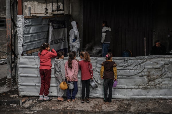 Four young girls holding buckets while waiting for food in Gaza.