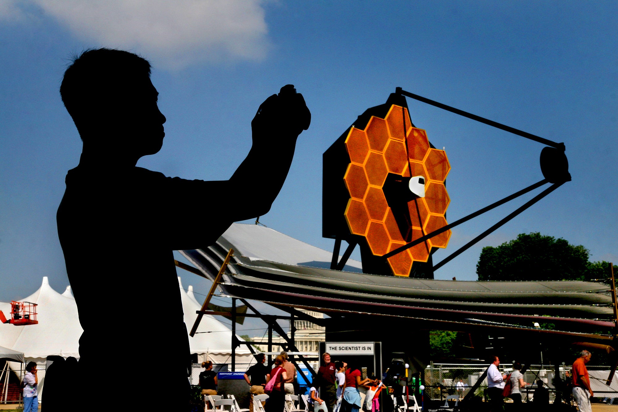 Silhouette of a visitor taking a photo, a full-size model of the James Webb Space Telescope is visible in the background on display outside of the National Air and Space Museum in Washington, D.C.