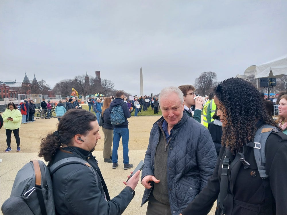 Un hombre parado afuera con un abrigo y el monumento a Washington al fondo.