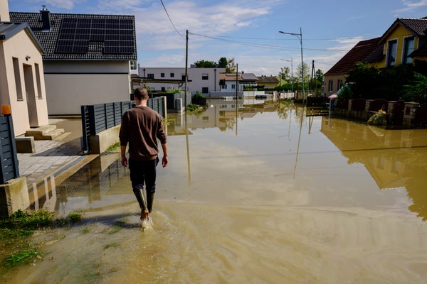 Man in knee high rain boots walks down a flooded residential street