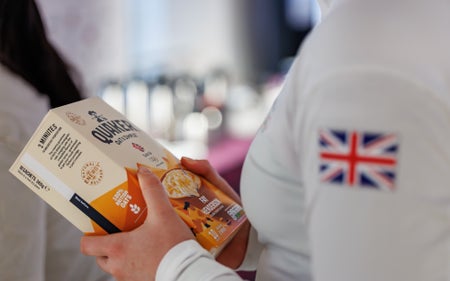 A woman in a white long-sleeved shirt with the Union Jack on the arm holds a box of Quaker Oats
