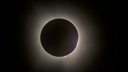 Total eclipse with several red bumps seen along the edge of the dark moon.