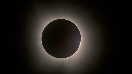 Total eclipse with several red bumps seen along the edge of the dark moon
