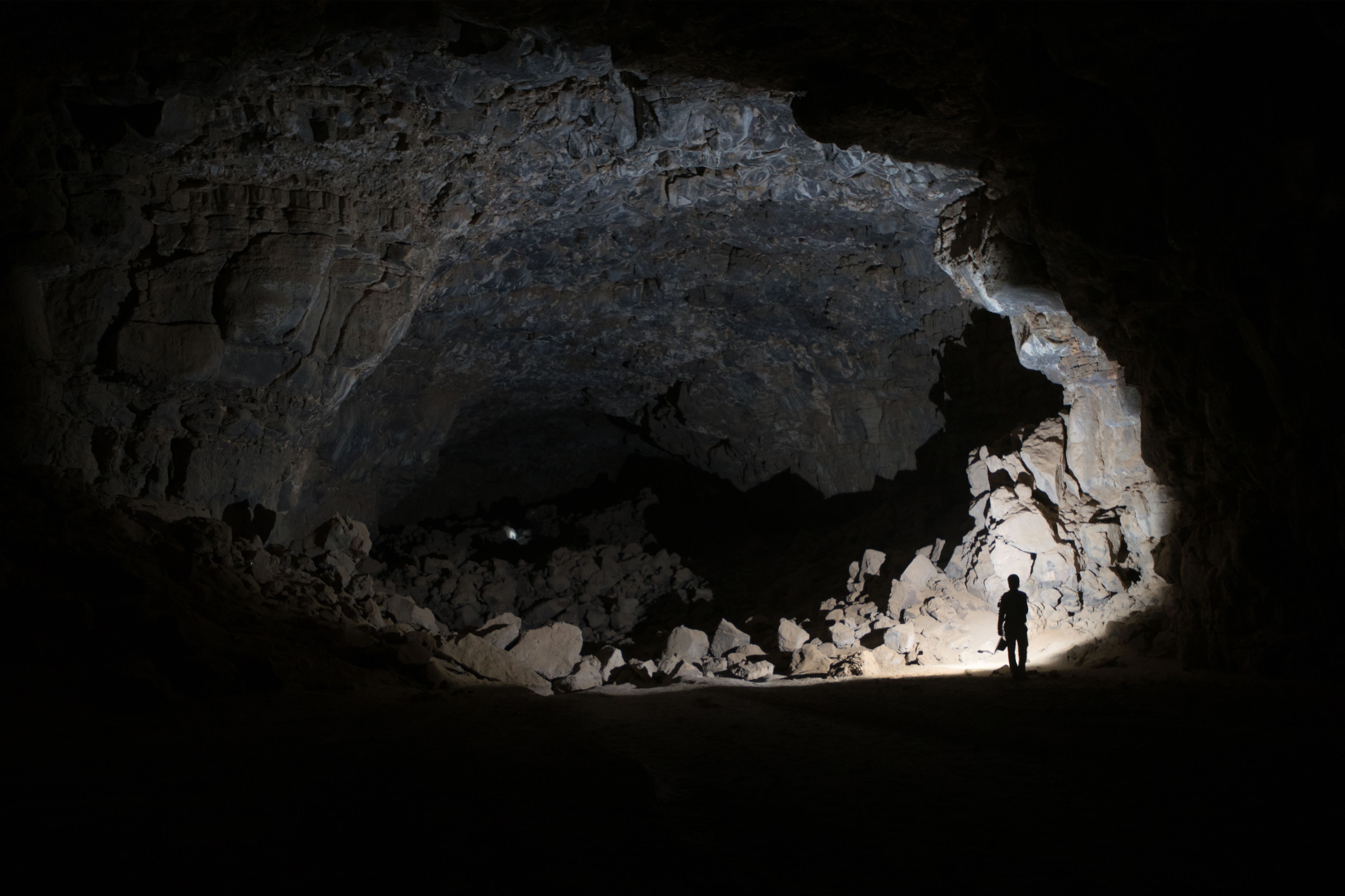 Person standing outside a circular cave entrance.