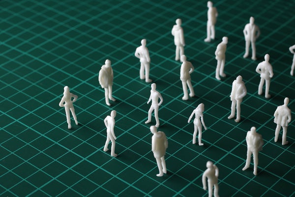 A large group of uncolored miniature human figurines stand in a grid formation on top of a green grid graphic