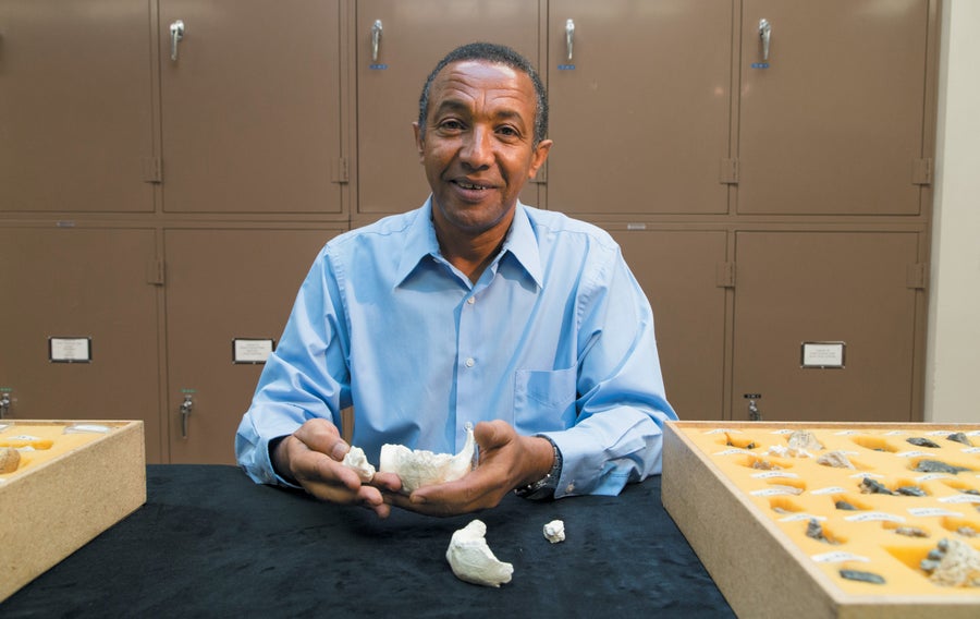 A man sitting in front of a row of lockers, with a small fossil in his hand