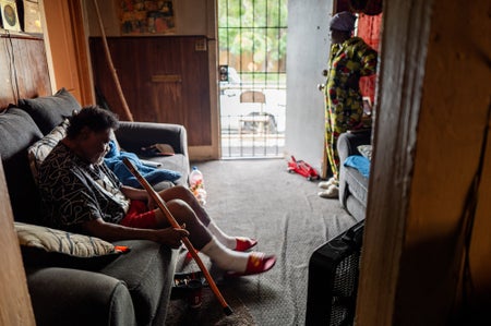 An interior photo showing a man siting on a couch and a woman looking our the front door of a home.