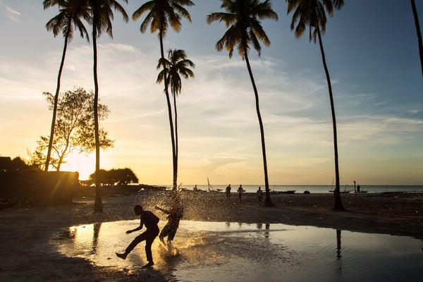 Children playing football in water on sunset near to beach with palm tree