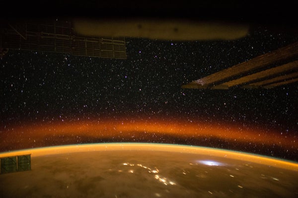 An amber sunset in Earth’s orbit captured from the International Space Station on April 18, 2015. A crimson aurora, as well as a thunderstorm and city illumination, are visible through the clouds.