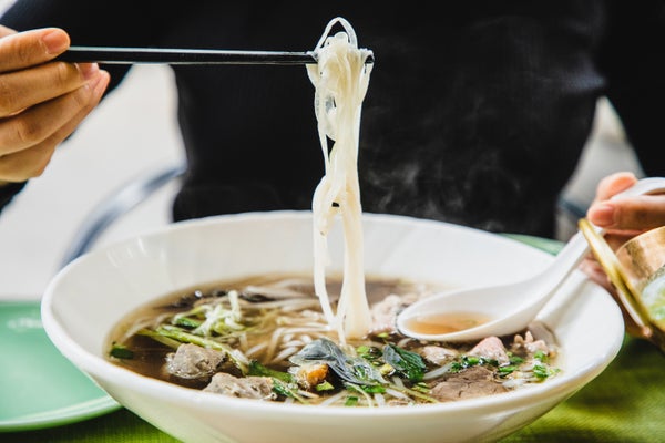 a person uses chopsticks to eat a big bowl of vietnamese pho