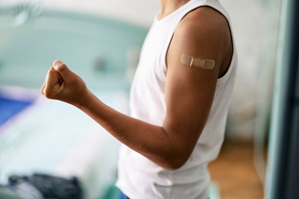 Teenager with white tank top showing vaccinated arm making a fist for power.