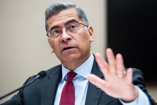 HHS Secretary Xavier Becerra in red tie and one hand up testifies.