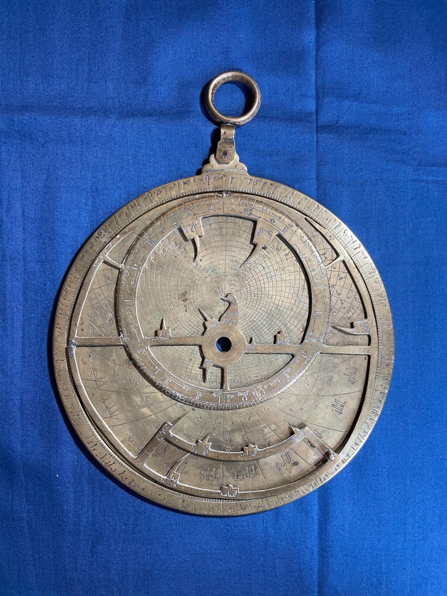 The Verona astrolabe laying on blue fabric. Inscriptions are carved into metal