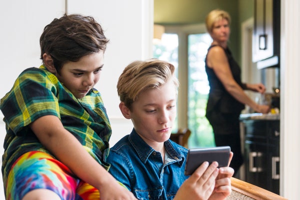 Mother with slightly concerned look on her face watching boys using the internet on a phone