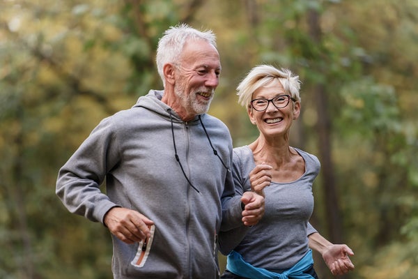A middle-aged man and woman running with trees behind them