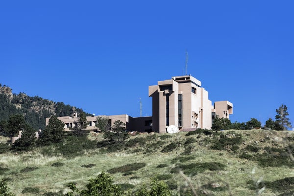 A blocky beige building atop a green hill with a blue sky in the background