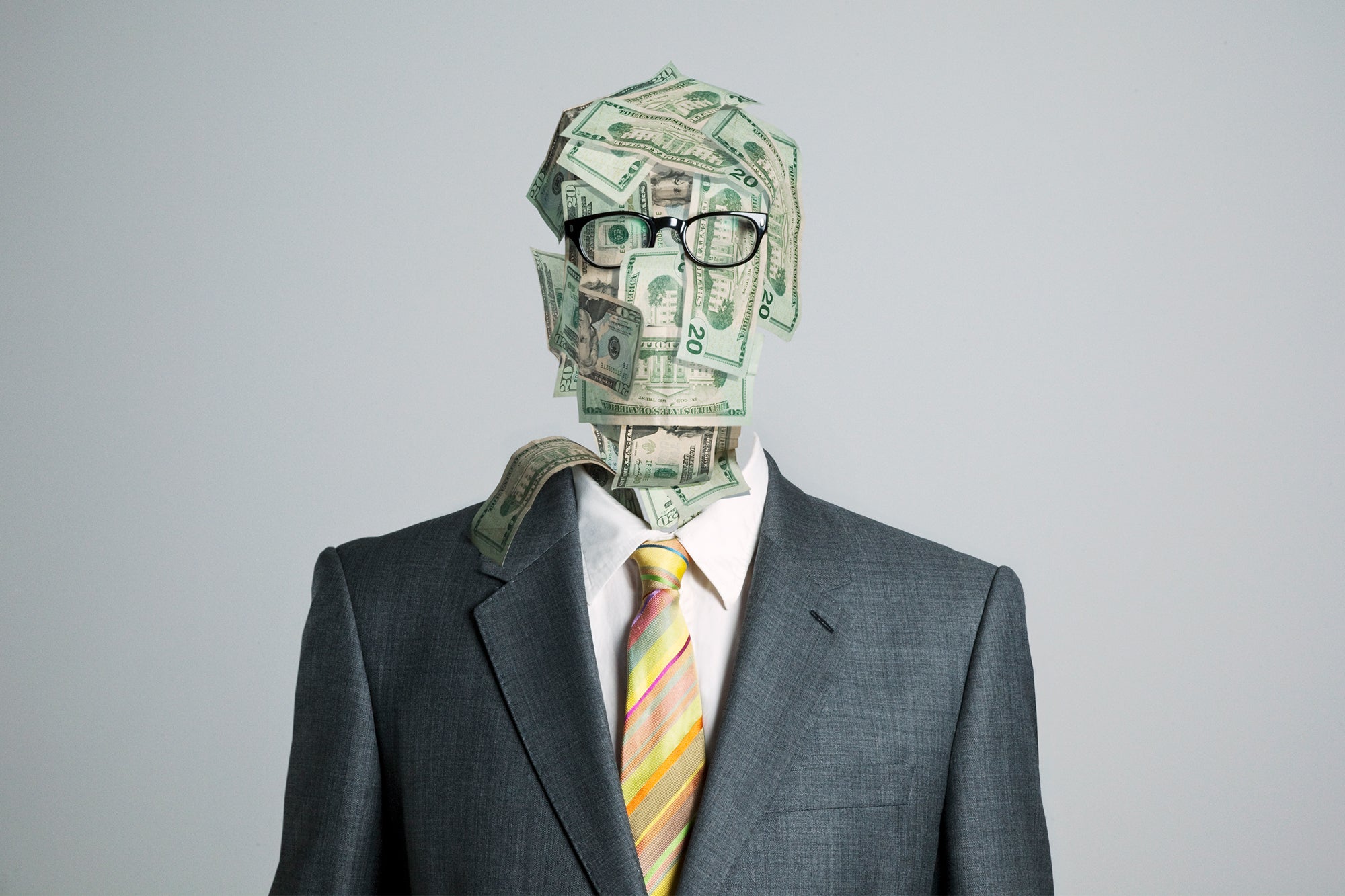Photo composite illustration, man made of money wearing glasses and a business suit on a gray background