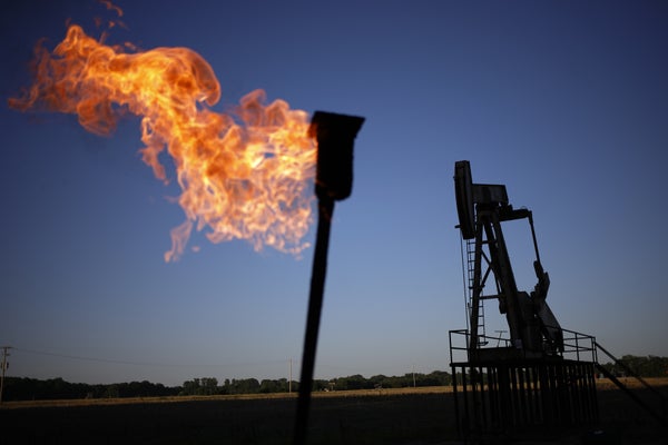A natural gas flare burns  next to an oil pump jack