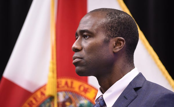 Florida state surgeon general Joseph Ladapo is pictured in profile standing in front of the Florida state flag