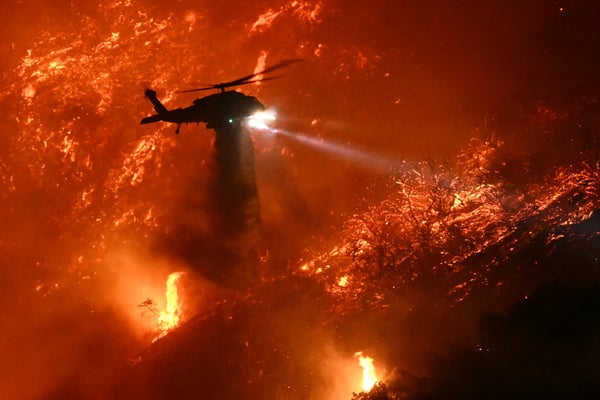 A fire fighting helicopter hovers above flames while dropping water