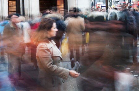 Woman standing still at Oxford square crossing while pedestrians are passing by, blurred motion due to long exposure