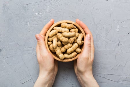 Female hands holding a wooden bowl with close peanuts.