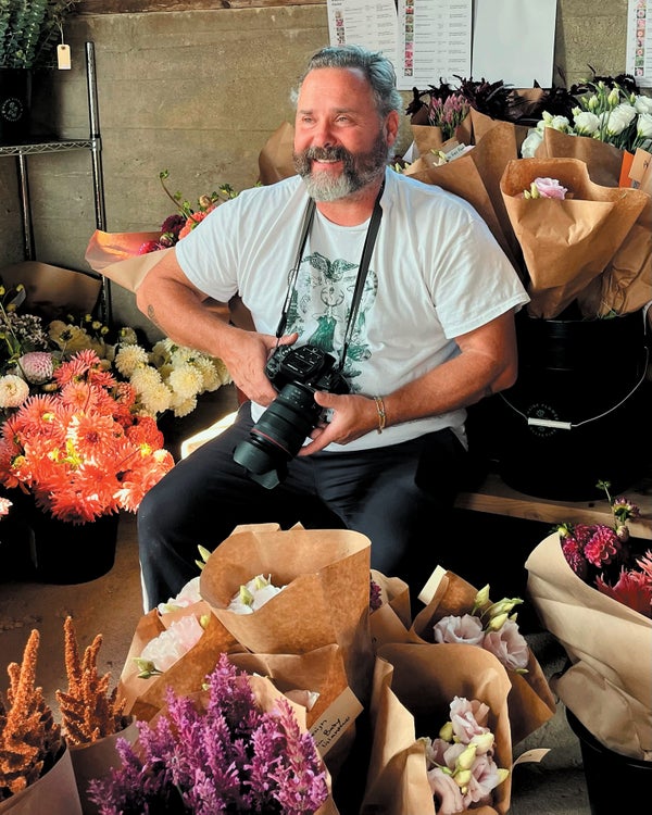 A man holding a camera, surrounded by flowers