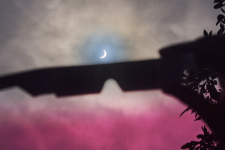 A pair of protective glasses is held up in silhouette against a cloudy sky during the solar eclipse of August 21, 2017 in California