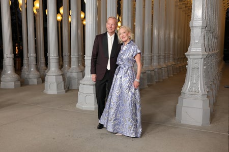 A man and woman in formal attire pose together in a dramatically lit, pillar-filled room.