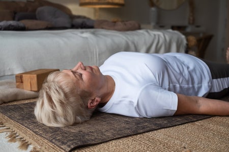 Senior woman laying flat on back on floor in bedroom at home