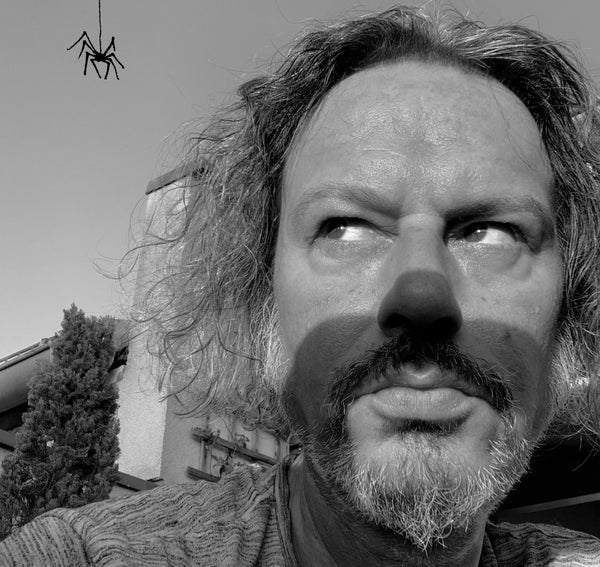 A black and white photo of a man (Thomas Fuchs) looking up at a hanging spider.