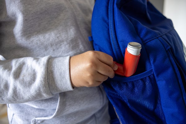 Unrecognizable 11-year-old asthmatic Caucasian schoolboy, packing his asthma inhaler into backpack