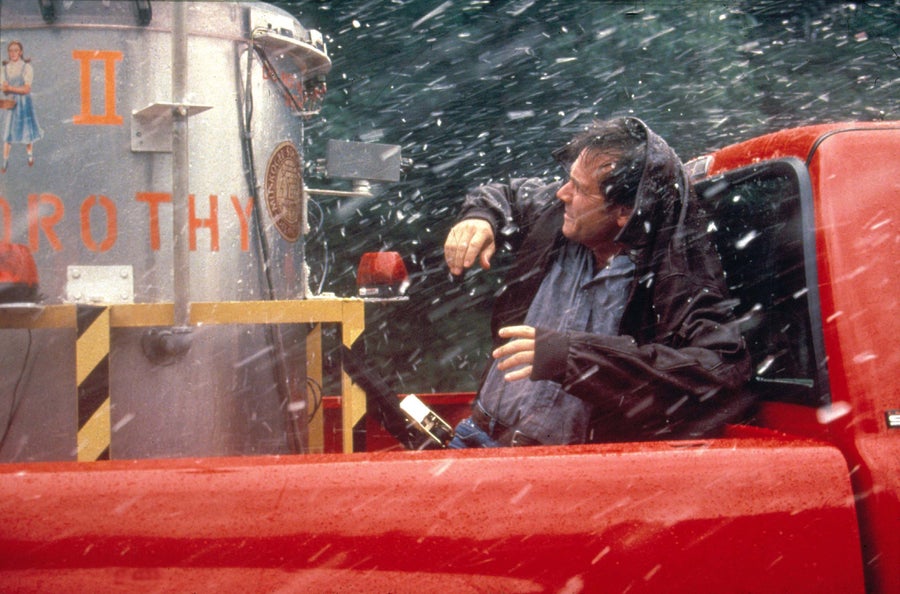 A movie scene depicting a man behind a red pickup truck during a hailstorm