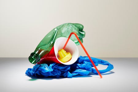 Common household plastic items balanced in a stack on a plain gray surface with a beige wall backdrop