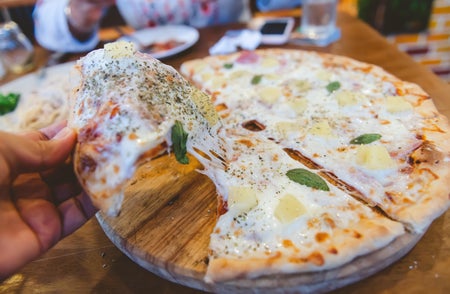 A hand pulls a slice of pizza out of a pie, showcasing the stretchiness of the cheese atop it.