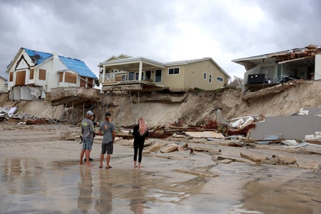 Four young people standing at the beach looking at three homes on top of washed away sand and damaged by the hurricane.
