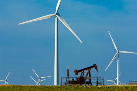 Blades of Wind Turbines surround Oil Well pumping unit in Agricultural Field.