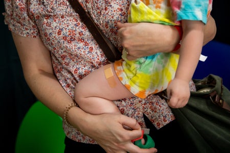 A person holding a child with a BandAid on their leg after receiving a covid vaccine.