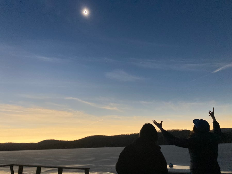 Two people from the back - one with hands reaching to the sky watching the eclipse.
