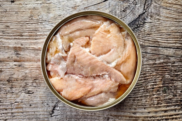 Open tin of canned salmon on wooden background
