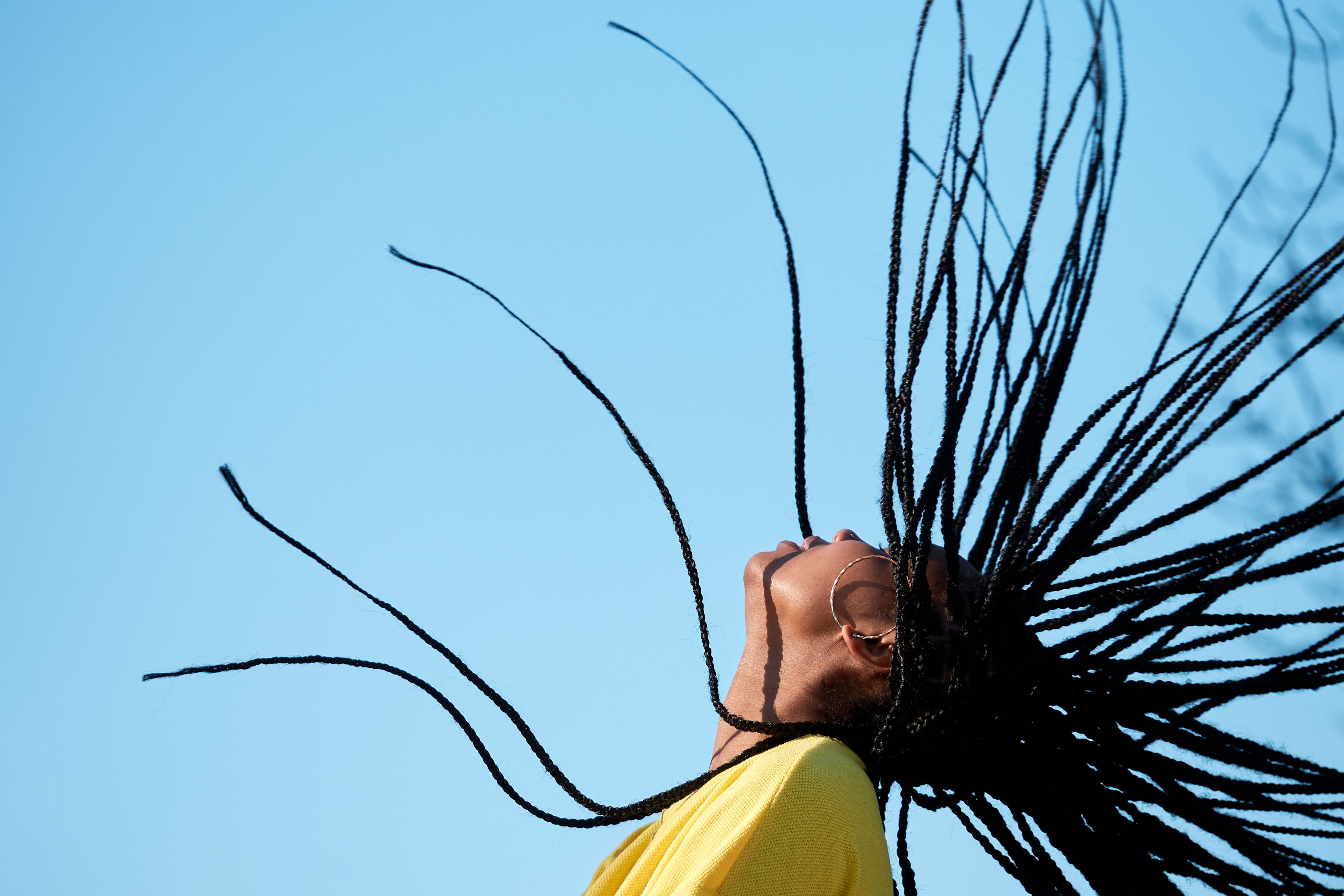 Motion shot of young, Black woman flipping dreadlocks back against blue sky background