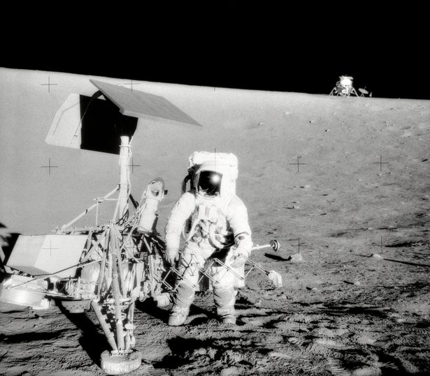 Archival black and white photo of astronaut examining spacecraft on the moon